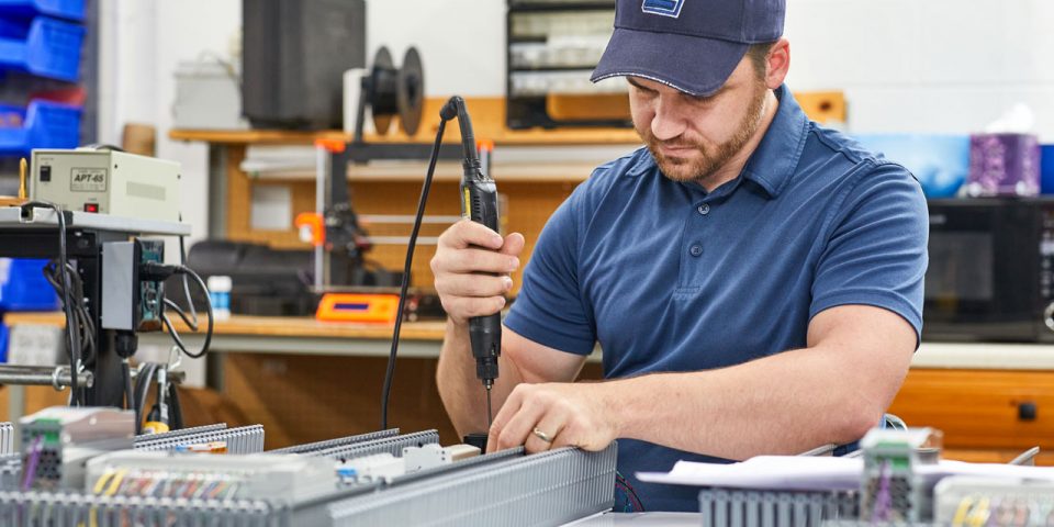 Man wearing a baseball cap adjusting components of a mechanical control board