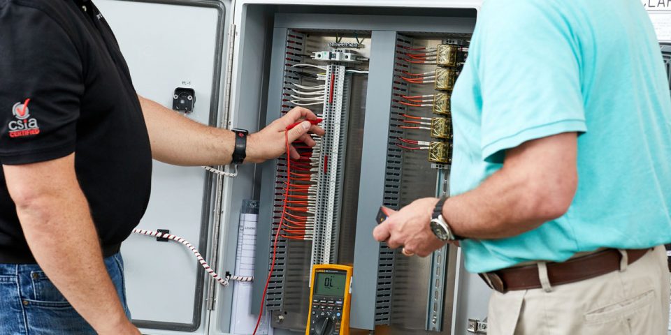 Two men looking at the inside of a large mechanical control panel