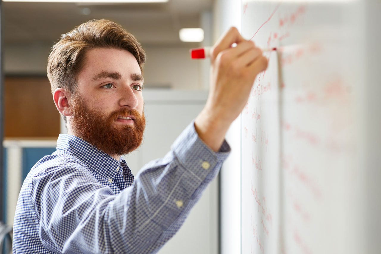 Young male professional with red hair and beard writing on a whiteboard