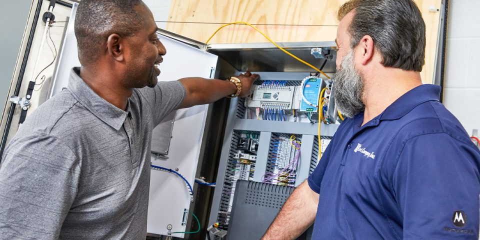 Two smiling men looking at the interior of a mechanical control panel